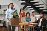 Man holding box of possessions leaving an office with colleagues