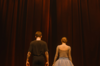 Two dancers standing behind a red stage curtain