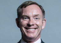 Chris Bryant smiles in front of a grey background