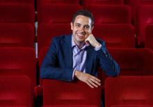 Lee Henderson sits on red seats in an auditorium