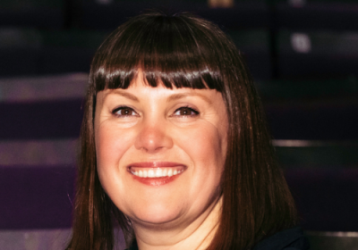 A headshot of Kate Denby, she smiles and has dark brown hair with a fringe