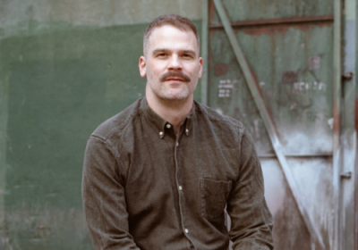 Kris Nelson sits in front of a rusty green door