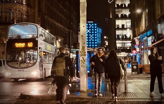 Buses passing and people crossing the street after dark