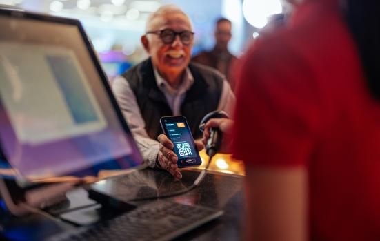 A senior Caucasian man is at the box office holding up his phone as the cashier is scanning the qr code