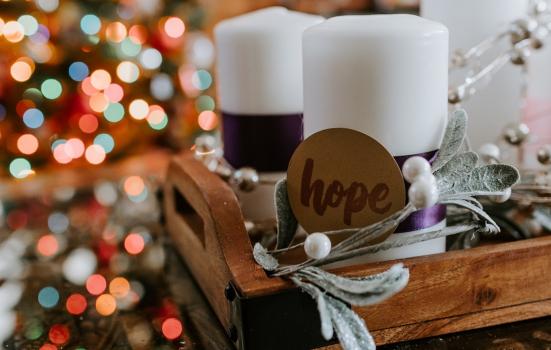 Candle with a brown card label saying hope attached, christmas decorations in the background