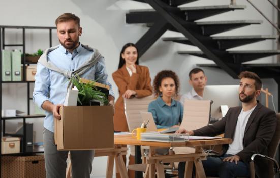 Man holding box of possessions leaving an office with colleagues