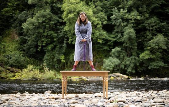 A woman in a dressing gown standing on a table by a river bed