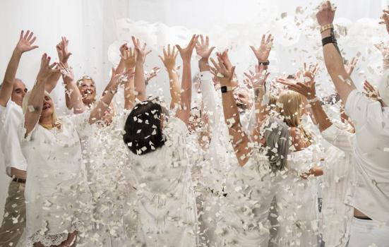 Image of people dressed in white, hands aloft, with white confetti/petals falling