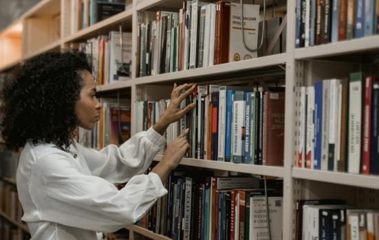 A woman looks through books on a library shelf