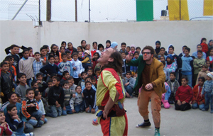 A man dressed as a jester, juggles in front of a group of children