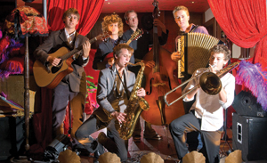 Siz young men in what looks to be a jazz band, in a room draped with brightly coloured material.