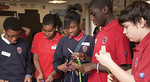 A group of teenagers in school uniforms take part in crafts in a classroom.