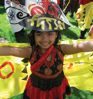 A little girl in a red costume and hat waving a big banner at the camera