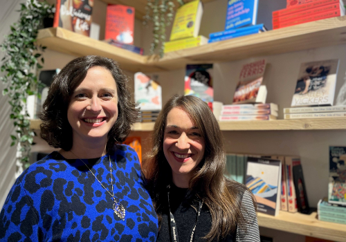 (L to R) Jemma Guerrier, Katie Clark. They are both smiling and have brunette hair. Books are in the background.