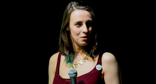 Florence Schechter MCing a Vagina Museum event, she has dark shoulder length hair and wears a red top.