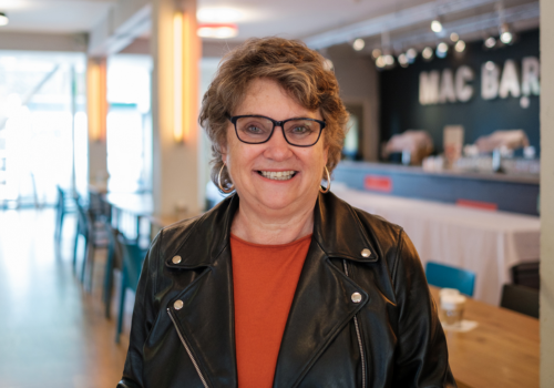 Ros Robins wears glasses, red top and a black leather jacket.