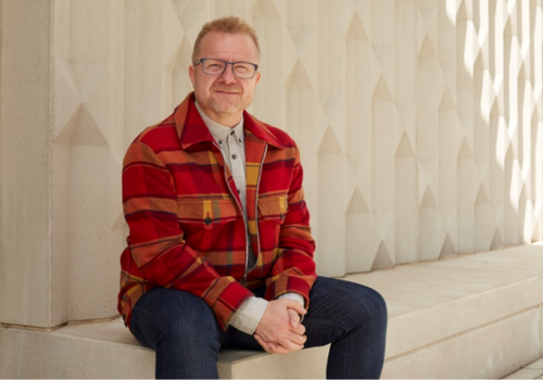 Tim Arthur sits on a bench in front of a white wall