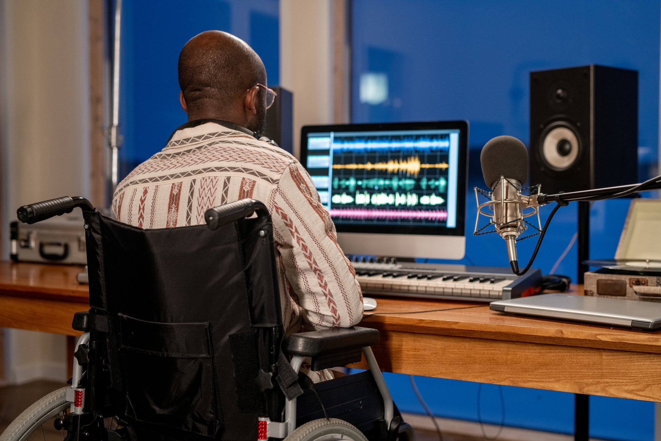 Man using sound recording program while sitting by table in front of computer monitor in studio